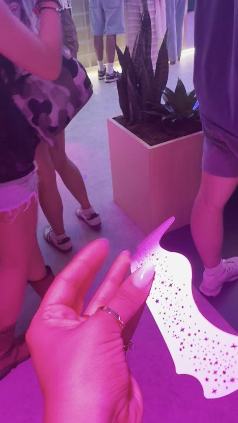A hand holding a Fazit glitter freckle makeup patch with star speckles under neon lighting inside the activation